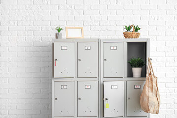 Modern locker with plants and bag near white brick wall