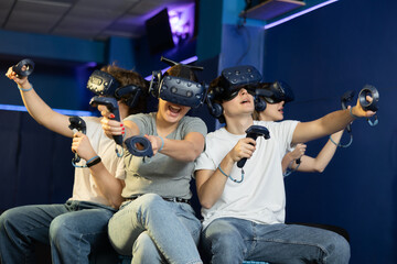 in computer club, group of four friends wearing virtual reality glasses and with joysticks are...