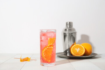 Glass of cold Negroni cocktail, oranges and shaker on light tile table