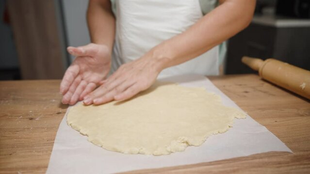 The woman shapes the dough into a round form on a baking paper, with a wooden rolling pin lying nearby.