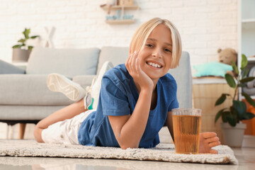 Little boy with glass of juice lying on floor at home