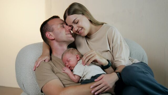 Happy Caucasian people sitting in the chair. Little newborn lies on the man's chest sleeping.