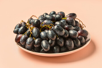 Plate with sweet black grapes on pink background