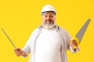 Portrait of senior man in hardhat with rasp and handsaw on yellow background. Labor Day celebration