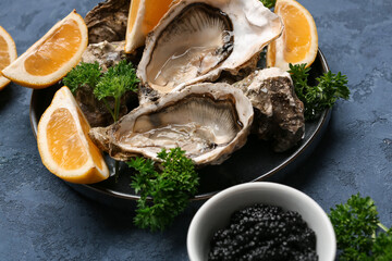Plate of tasty oysters with lemon and black caviar on blue background