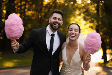 Happy newlywed couple with cotton candies in park
