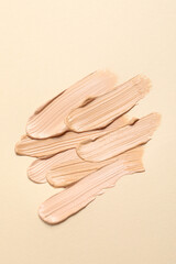Samples of skin foundation on beige background, top view