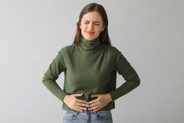 Young woman suffering from stomach ache on light background