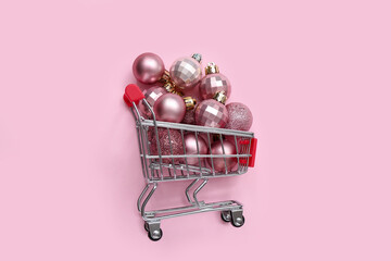 Small shopping cart with different Christmas balls on pink background