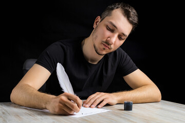 Young handsome and serious man dressed in black quill pen writes on white sheet of paper on black...