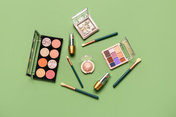 Beautiful palettes of eyeshadows and different decorative cosmetics on green background - obrazy, fototapety, plakaty