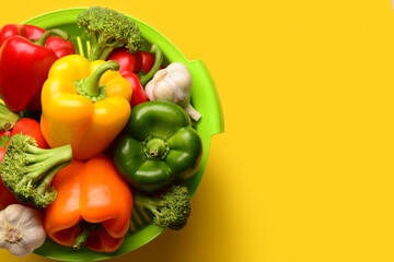 Colander with different fresh vegetables on yellow background