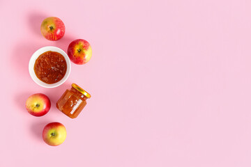Bowl and jar of sweet apple jam on pink background