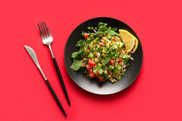 Plate with delicious tabbouleh salad and cutlery on red background