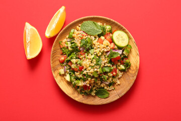 Plate with delicious tabbouleh salad and lemon pieces on red background