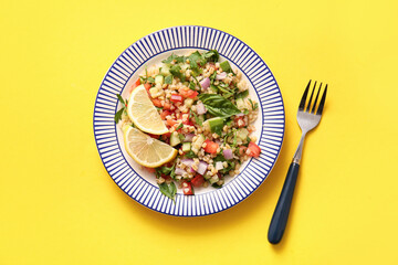 Plate with delicious tabbouleh salad and lemon slices on yellow background