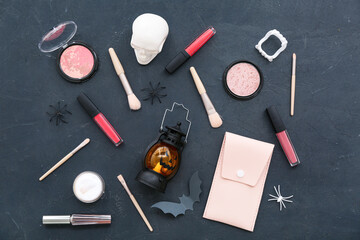 Composition with different makeup products and Halloween decor on black background