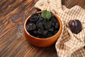 Bowl with tasty dried plums on wooden background