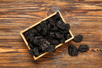 Box with tasty dried plums on wooden background