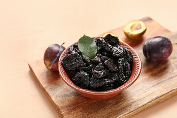 Bowl with tasty dried plums on orange background