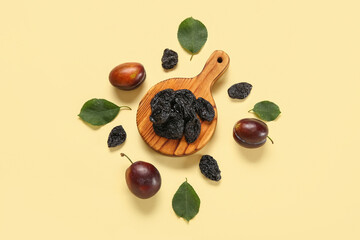 Wooden board with tasty dried plums and fresh fruits on yellow background