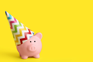 Piggy bank in party hat on yellow background - obrazy, fototapety, plakaty