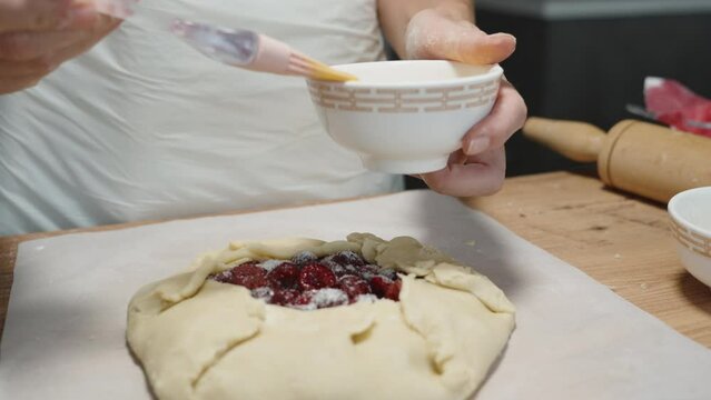 The woman is brushing the dough of the cherry galette with egg for a crispy crust.