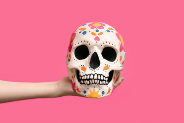 Female hand holding painted human skull for Mexico's Day of the Dead (El Dia de Muertos) on pink...