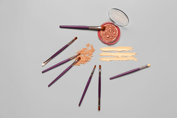 Makeup brushes and different decorative cosmetics on grey background