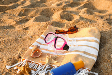 New swimming mask, towel, starfishes, sunglasses, sunscreen cream and seashell on sand