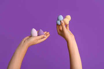 Female hands with different makeup sponges on purple background