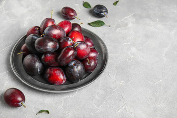 Plate with fresh ripe plums and leaves on grey background