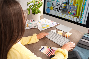 Female interior designer working with computer at table in office - obrazy, fototapety, plakaty