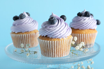 Stand of tasty cupcakes with blueberries on blue background
