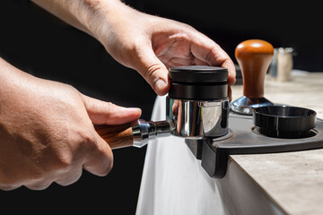 The Barista hand uses the tamper to press fresh ground coffee into the portafilter
