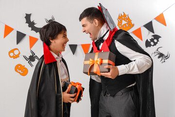 Little boy and his father dressed for Halloween as vampires with gifts on light background