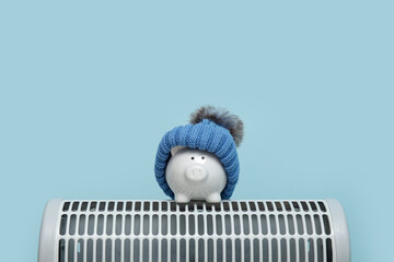 Electric convector heater, piggy bank and hat on blue background. Heating season