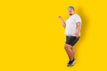 Fototapeta na wymiar Happy Asian overweight guy dancing isolated over yellow background