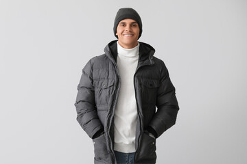 Young man in warm puffer jacket on light background