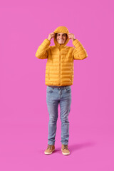 Young man in warm puffer jacket on purple background