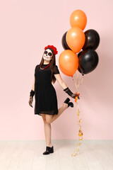 Young woman dressed for Halloween with balloons near light wall