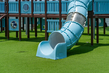 Blue children's slide on artificial green grass on a playground in a city park at a resort. It's hot sunny weather outside.