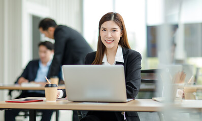 Portrait shot of Asian professional successful female businesswoman secretary employee in formal suit sitting smiling look at camera working laptop notebook computer at desk in company office