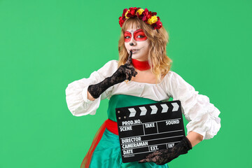 Young woman with painted skull on her face and clapperboard against green background. Halloween...