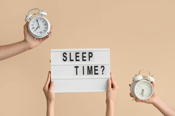 Hands holding alarm clocks and board with question SLEEP TIME? on beige background