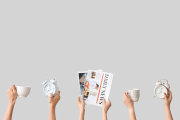Hands holding alarm clocks, newspapers and cups on grey background