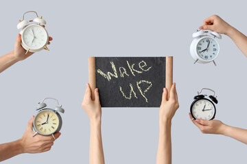Hands holding different alarm clocks and board with text WAKE UP on grey background