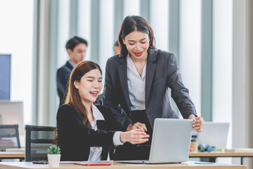 Asian professional successful female businesswoman supervisor mentor in formal suit standing smiling pointing help advising new colleague working with paperwork document at working station in office