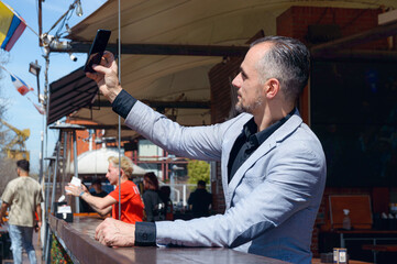 adult business man in elegant jacket suit taking selfie with his phone sitting outside restaurant