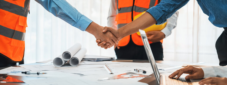Construction engineer handshake with businessman contractor over architecture design blueprint on meeting table. Architect and engineer shake hand after successful cooperation teamwork. Insight
